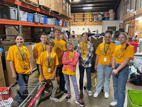 Several students in yellow shirts standing in a warehouse for a service project.